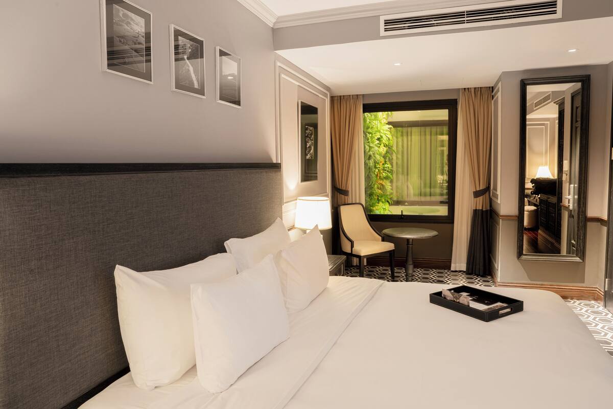 Ein Hotelzimmer mit einem großen Bett, einem kleinen Tisch, einem Stuhl und Blick auf Grünfläche.