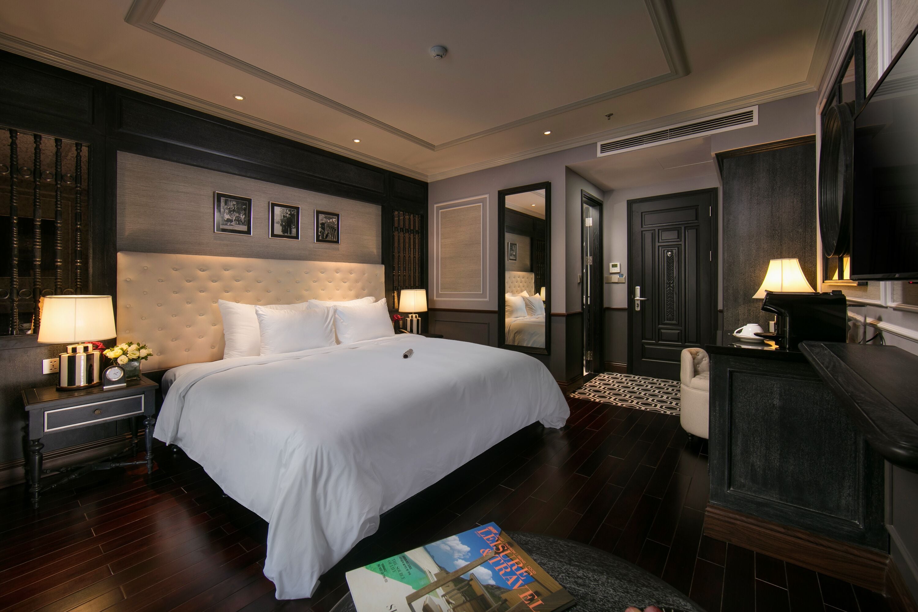 A hotel room with a large bed, a flat-screen TV, a desk with a lamp, and a mirror.