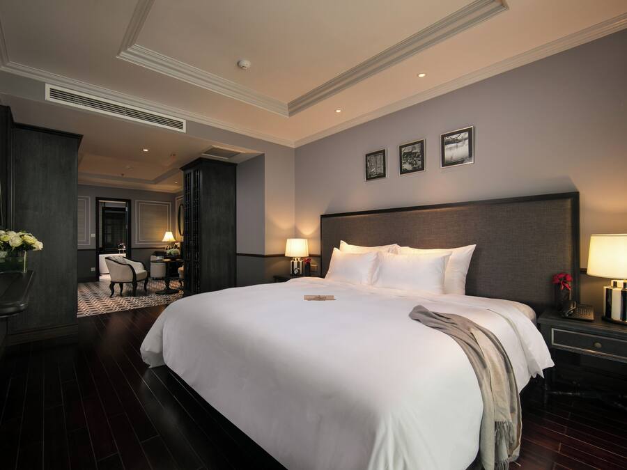 Ein Hotelzimmer mit einem großen Bett, zwei Nachttischen mit Lampen, einem Schreibtisch mit Stuhl und einer kleinen Sitzecke mit Sessel und Tisch.