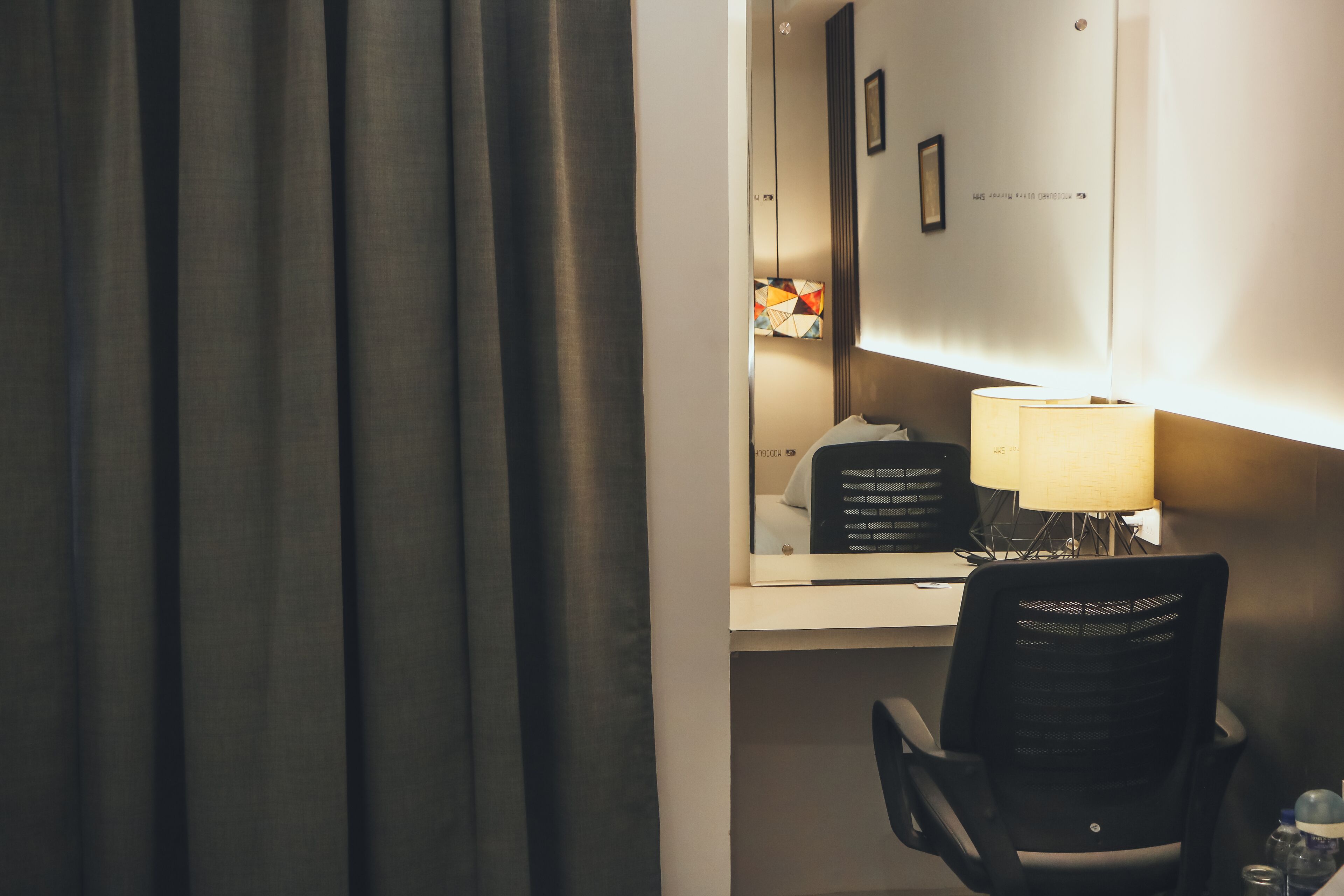 A hotel room with a desk, chair, lamp, and a large window with curtains.