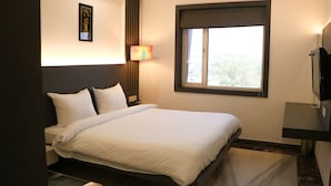 A hotel room with a bed, a bedside table, a lamp, a TV, and a window with a view.