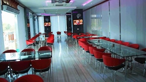 A modern conference room with glass tables and red chairs, equipped with ceiling fans and a large screen.