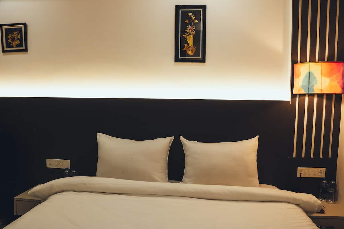 Ein ordentlich bezogenes Bett mit weißen Laken, einem schwarzen Kopfteil und einer Wandlampe.