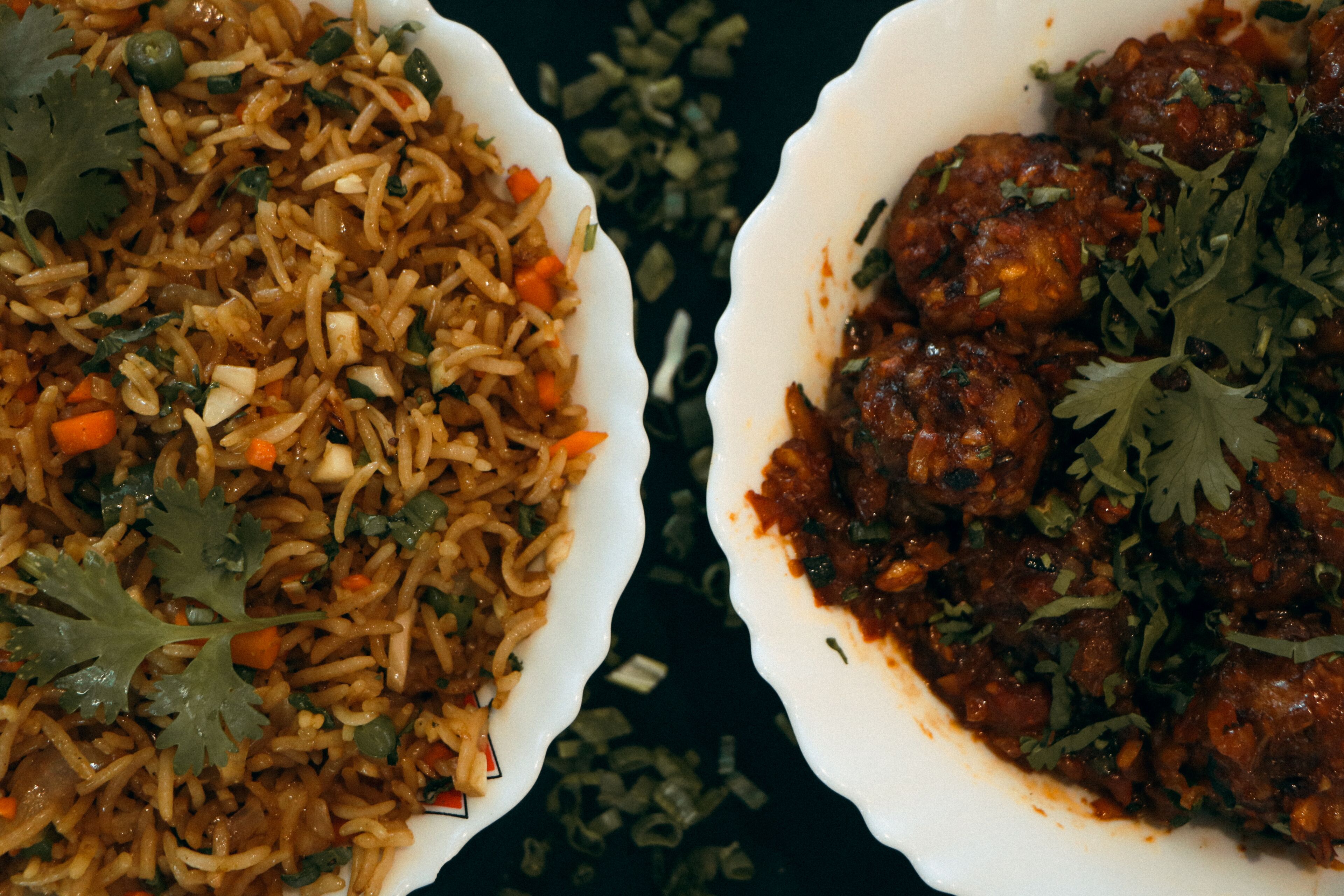 Two bowls of food, one with rice and vegetables and the other with a meat dish, both garnished with herbs.