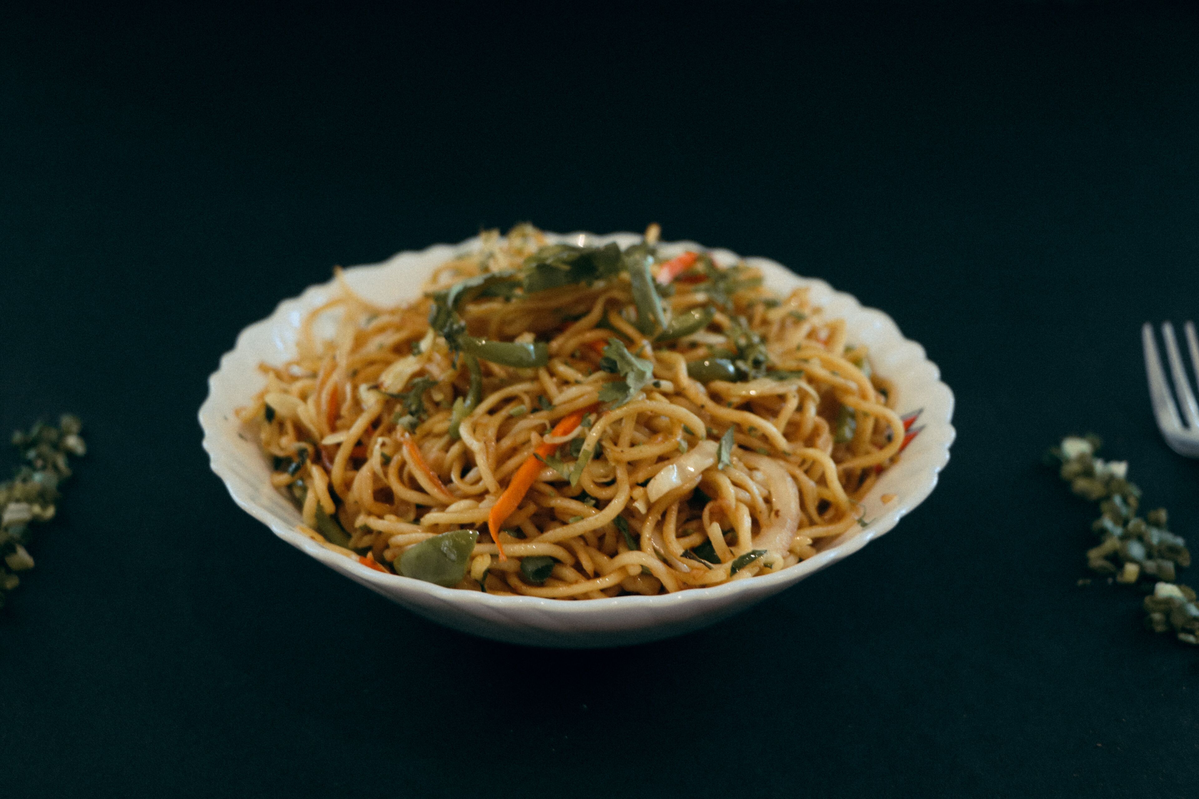 Un tazón de fideos con verduras sobre una superficie oscura.
