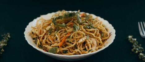 Un tazón de fideos con verduras sobre una superficie oscura.