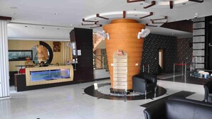 A hotel reception area with a modern design, including a reception desk, a large cylindrical column, and black leather seating.