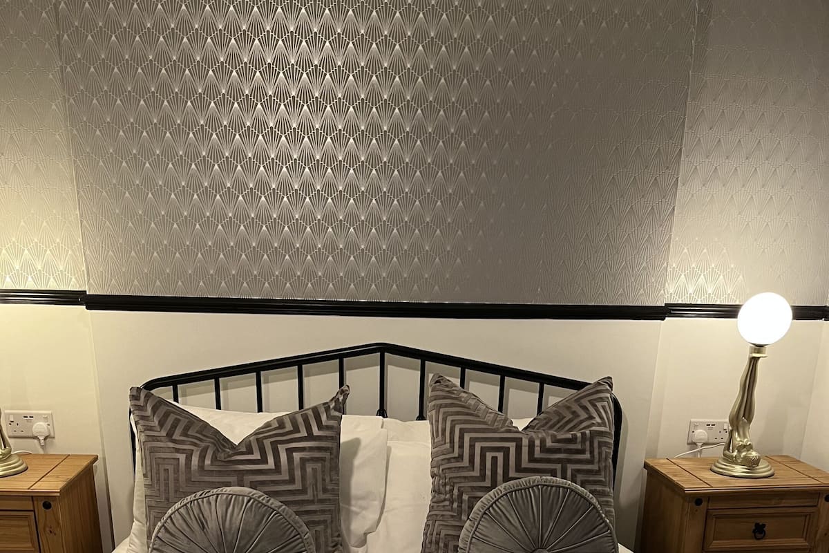 A neatly made bed with patterned pillows, a bedside lamp, and a wooden nightstand.