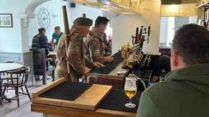 A bar area with a counter and stools, a clock on the wall, and a person seated at a table. - Tontine Hotel & Bar (Telford)