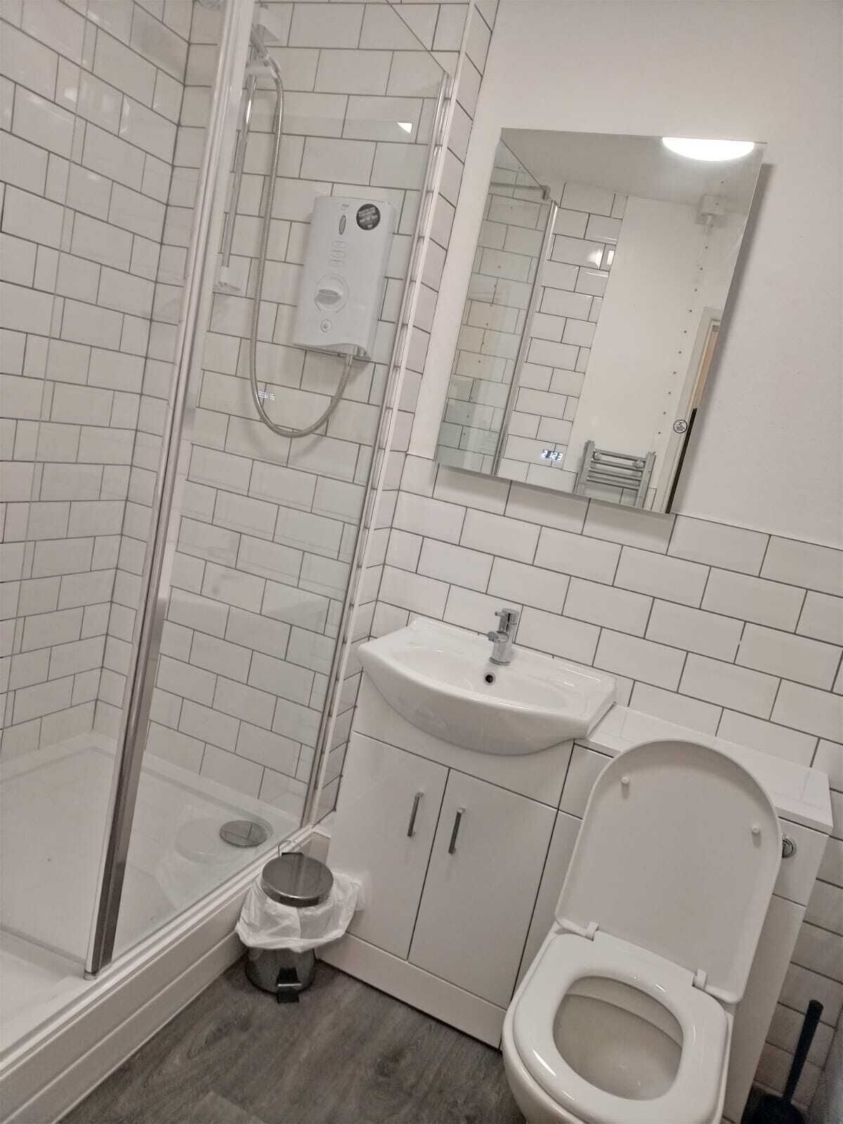 Ein Badezimmer mit Duschkabine aus Glas, Waschbecken und Toilette.