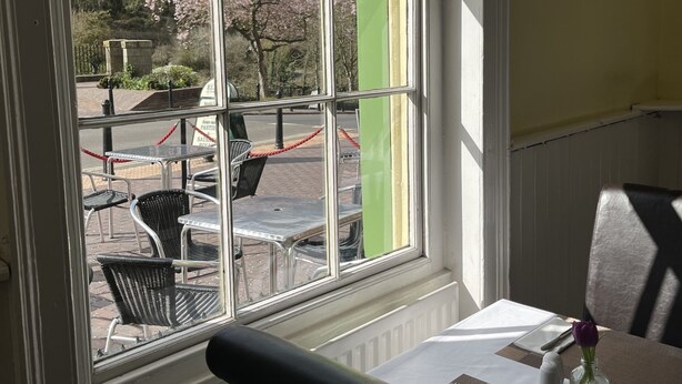 A dining area with a table set for two, a window with a view of cherry blossoms, and a green column. - Tontine Hotel & Bar (Telford)