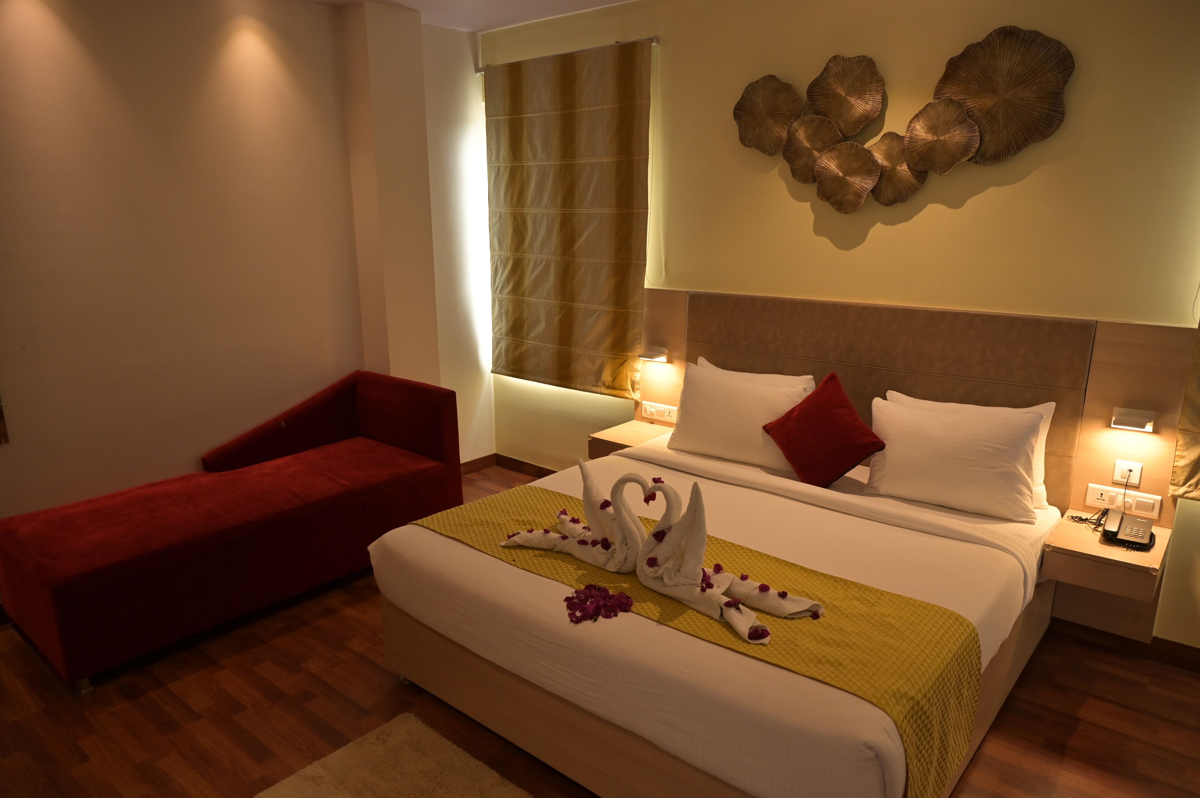 Une chambre d’hôtel avec un grand lit, un fauteuil rouge, un élément décoratif fixé au mur et une table de chevet avec une lampe.