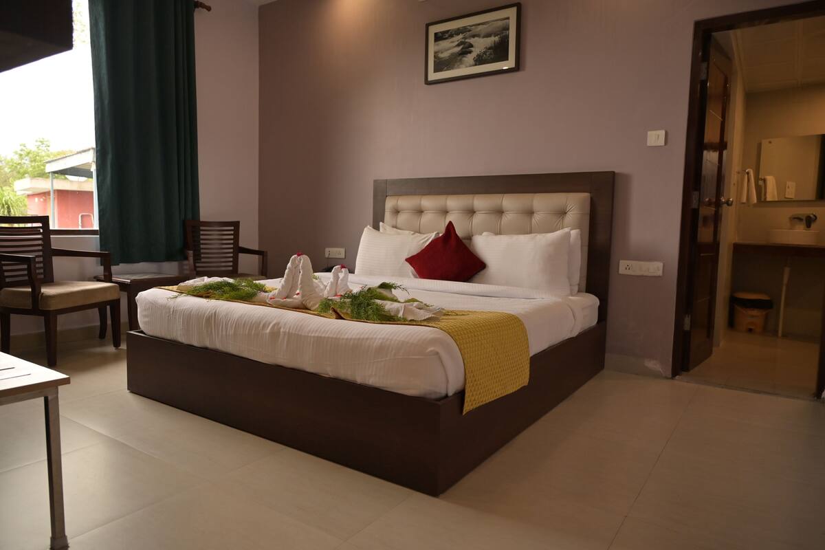 A neatly arranged hotel room with a large bed, a bedside table, a chair, and a view of the outside through a window.