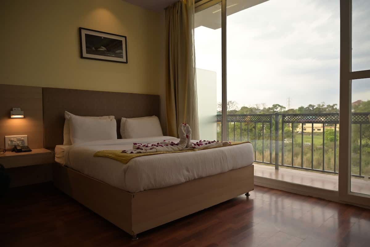 A hotel room with a large bed, a nightstand, a bedside lamp, and a view of the outdoors through a large window.