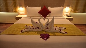 Habitación de hotel con una cama bien hecha, un almohadón rojo y un cisne decorativo hecho con toallas sobre la colcha.