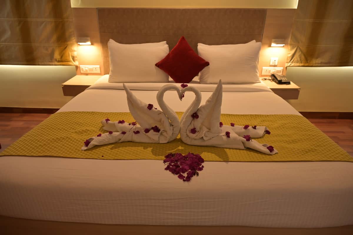 A hotel room with a neatly made bed, a red pillow, and a decorative swan made of towels on the bedspread.