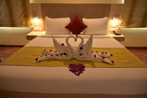 Habitación de hotel con una cama bien hecha, un almohadón rojo y un cisne decorativo hecho con toallas sobre la colcha.
