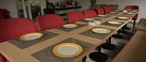 Un salón de conferencias con una larga mesa dispuesta para una reunión, equipado con sillas y cubiertos.