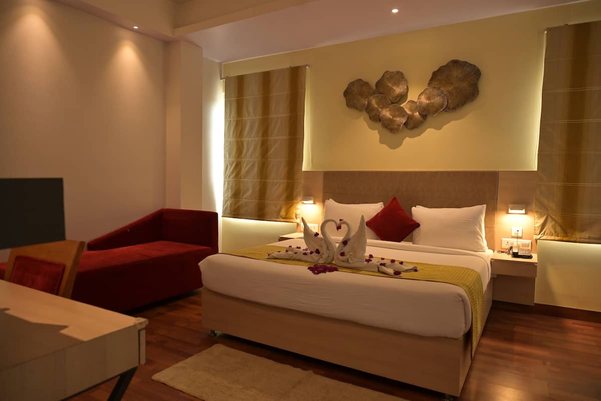 A modern hotel room with a large bed, red armchair, and a decorative wall piece above the bed.