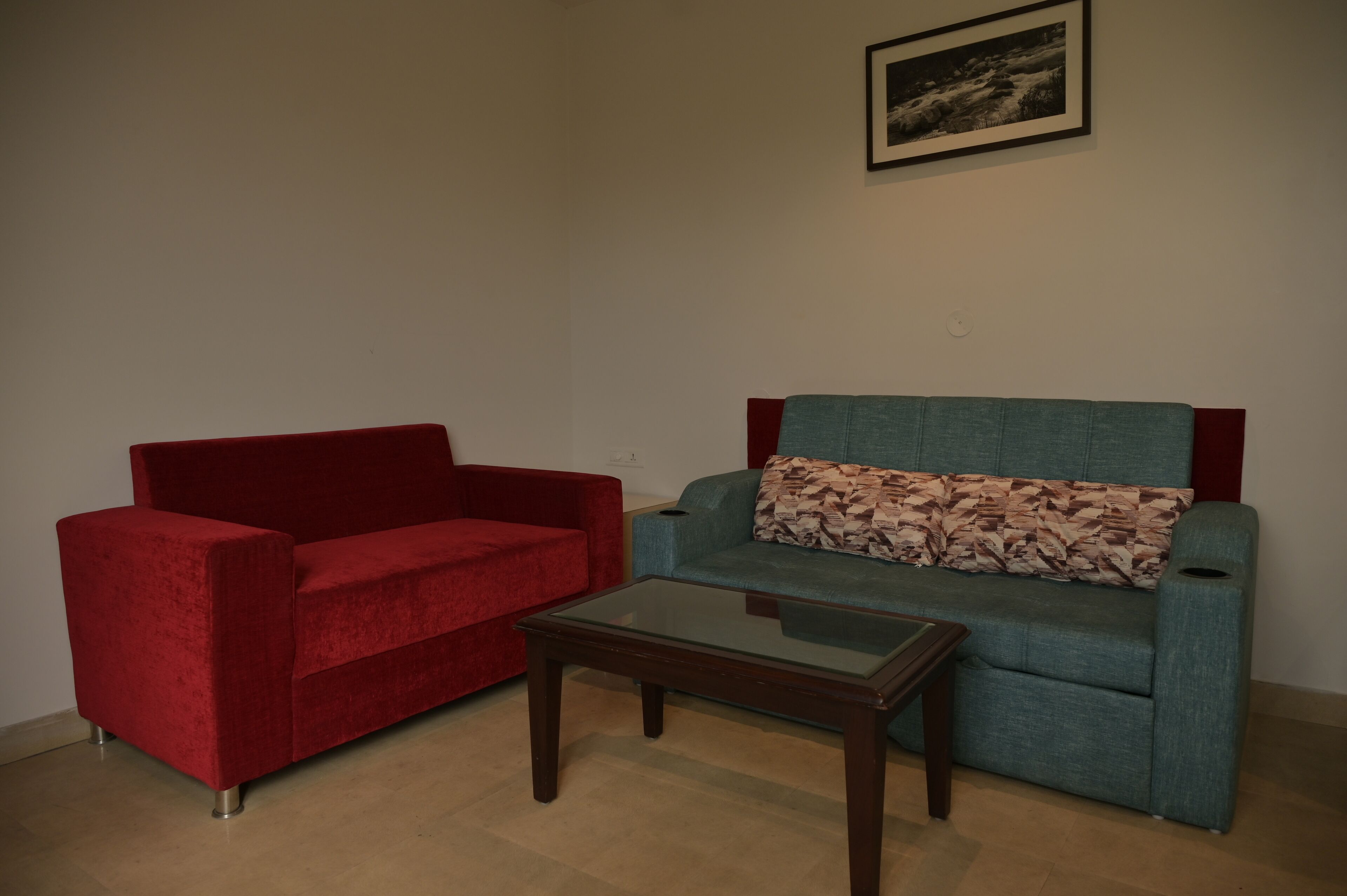 Une pièce avec un canapé rouge, un canapé turquoise orné d’un coussin à motifs et une table basse en verre.