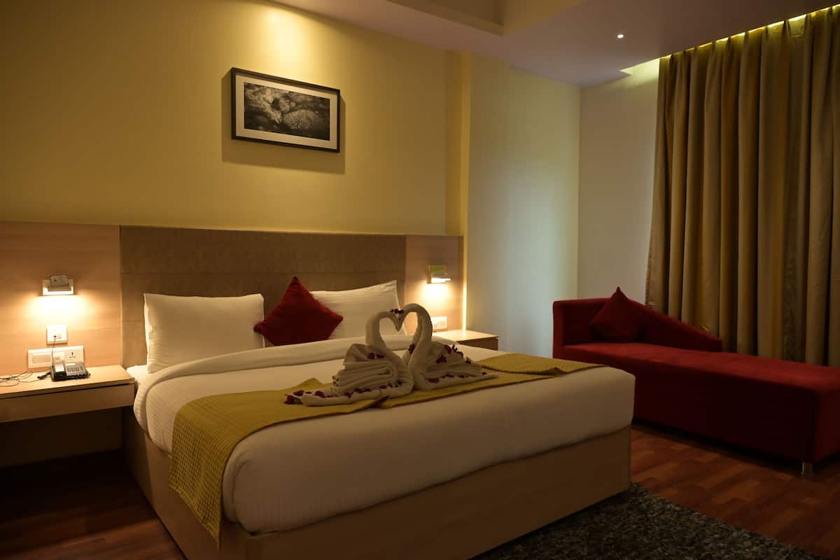 A hotel room with a large bed, a red sofa, a headboard with a picture, and a curtain.