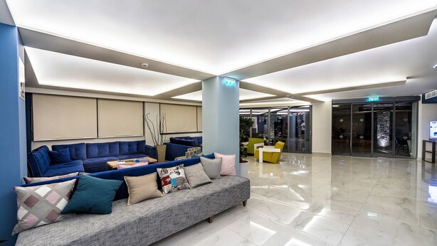 A modern lobby with a grey sofa, blue and yellow seating, and a polished marble floor. - Pollis Hotel (Hersonissos)
