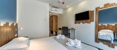 A hotel room with a large bed, a desk, a chair, a TV, and a mirror.