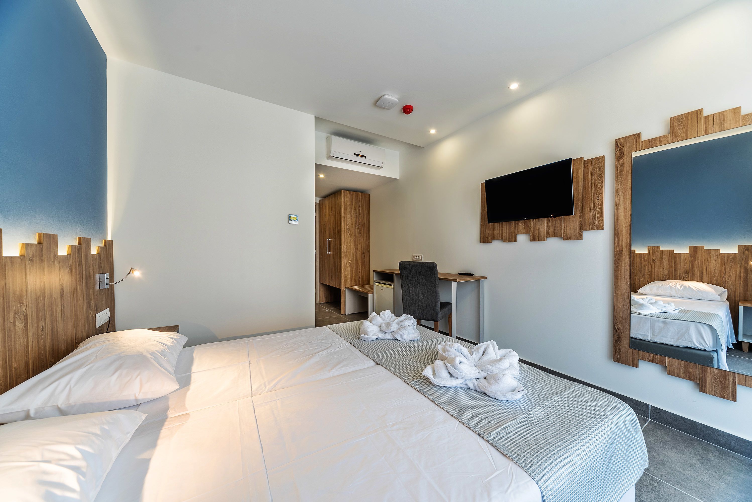 Habitación de hotel con una cama grande, un escritorio, una silla, un televisor y un espejo.