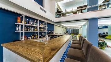 Zona de bar moderna con barra de madera, asientos y una variedad de botellas de licor en estantes.