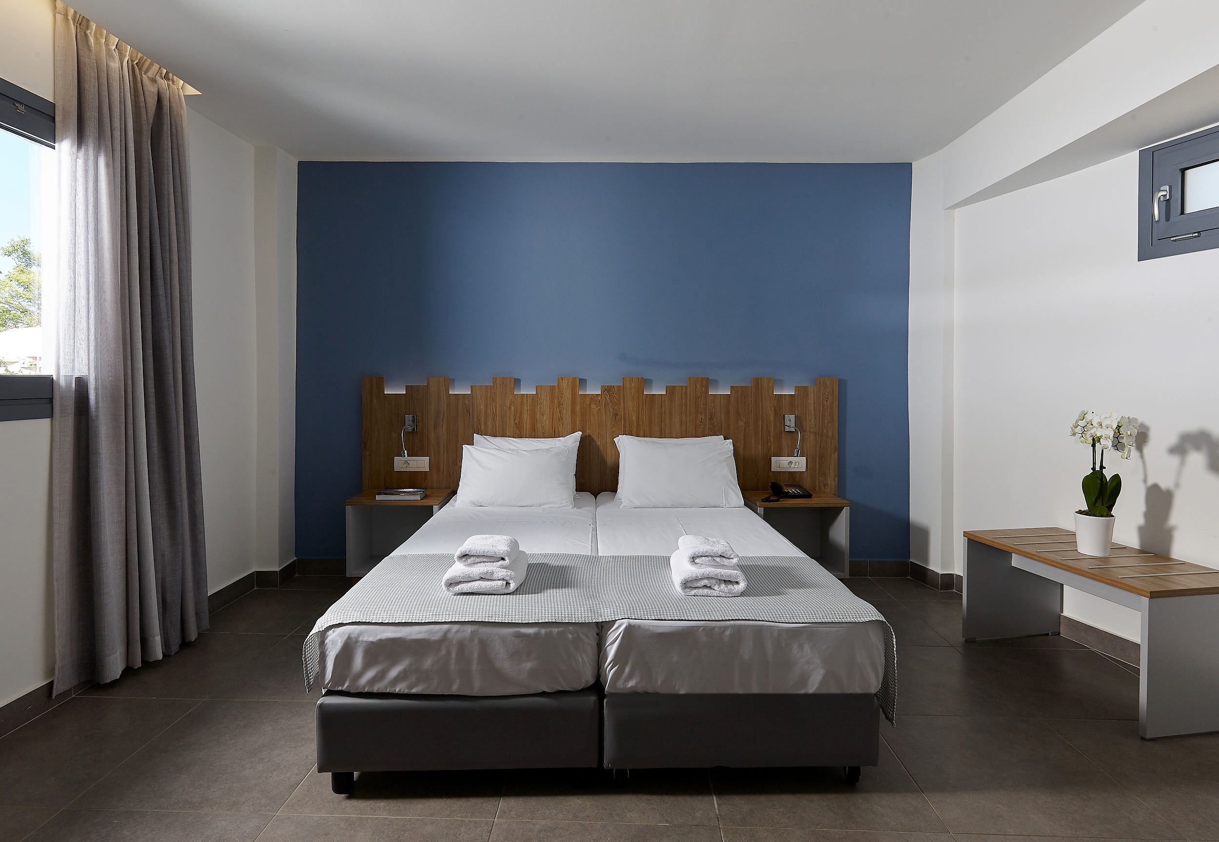 A double bed with two pillows, a wooden headboard, a bedside table, and a bench.