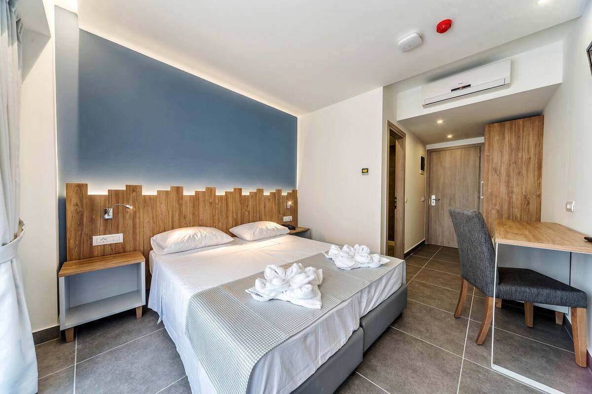 A modern hotel room with a large bed, a desk, and a wardrobe.