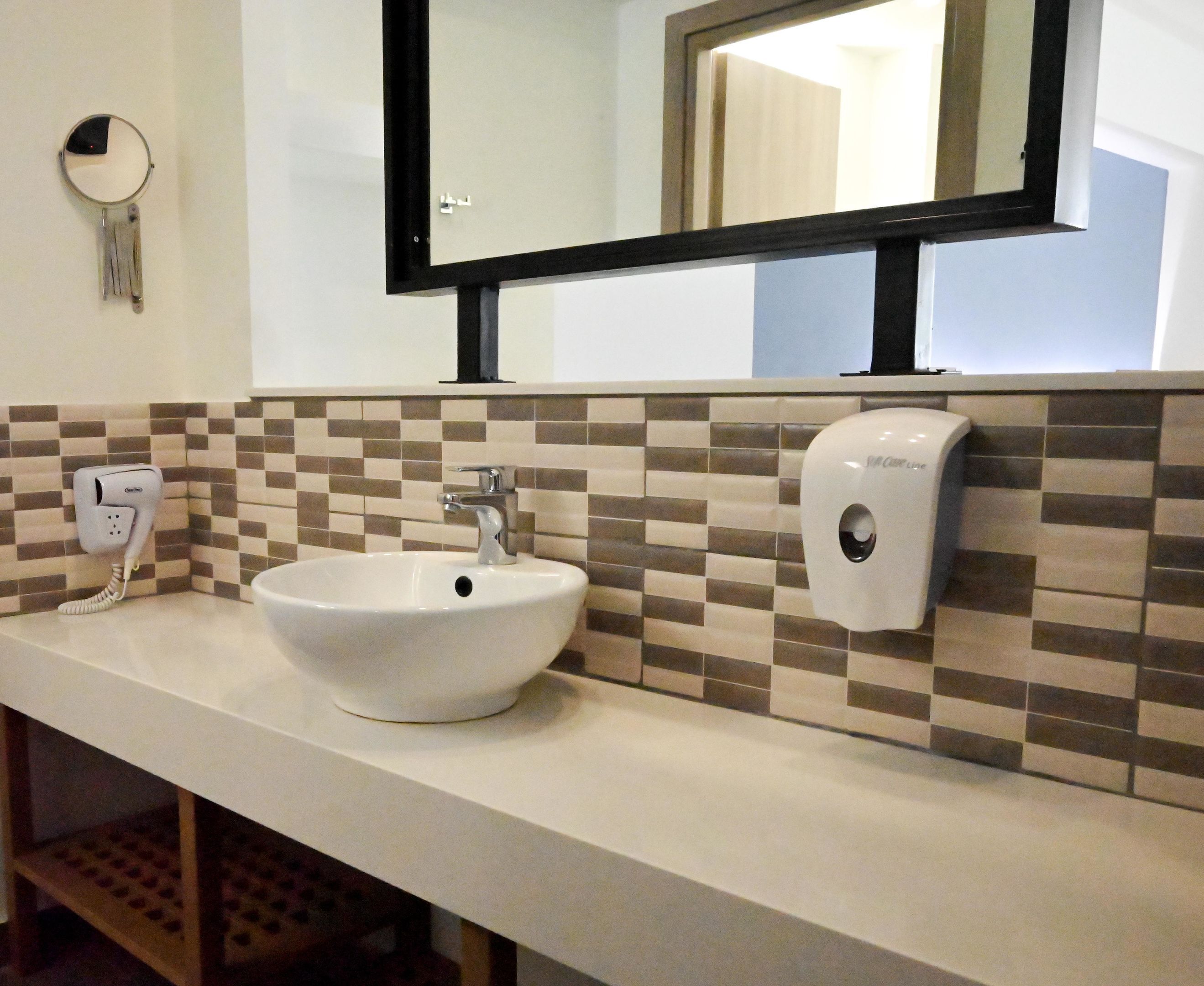 Une salle de bain avec un lavabo blanc, un miroir, un distributeur de savon et un sèche-cheveux fixé au mur.