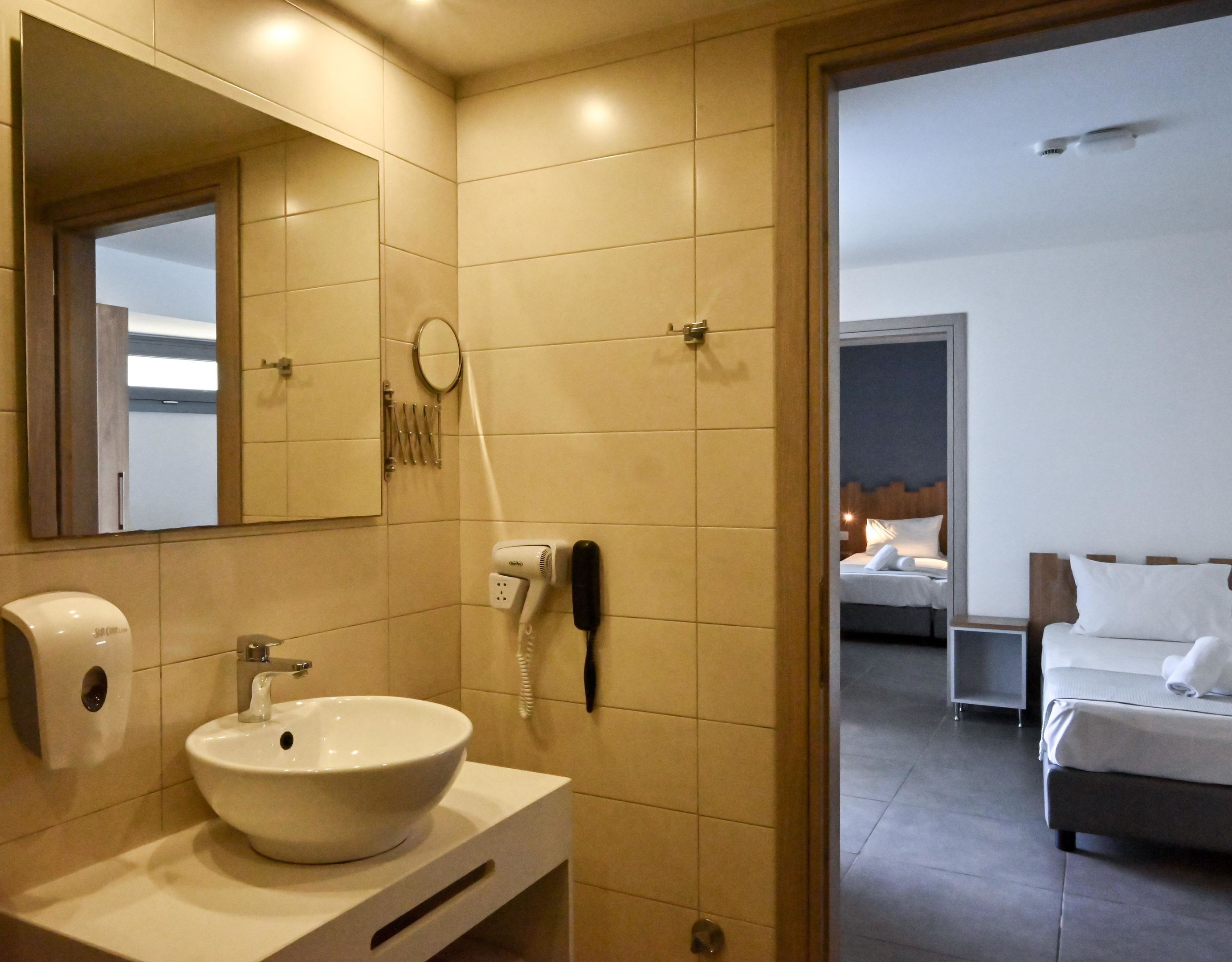 A hotel bathroom with a sink, mirror, hairdryer, and phone.