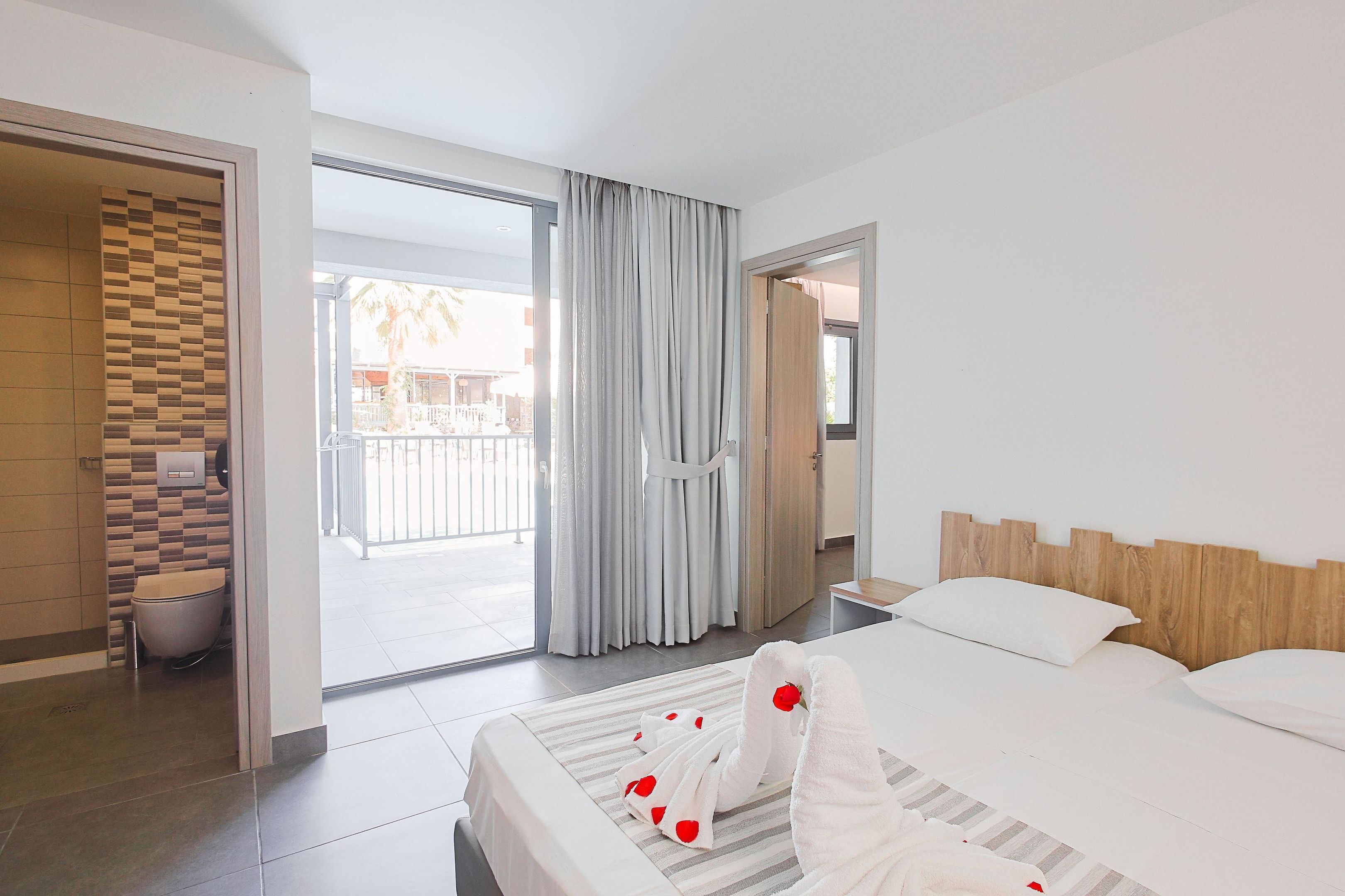 Habitación de hotel con una cama grande, baño y balcón con cortinas.