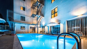 Una piscina con escalera metálica, un escape de incendios y un edificio con ventanas grandes y una puerta.