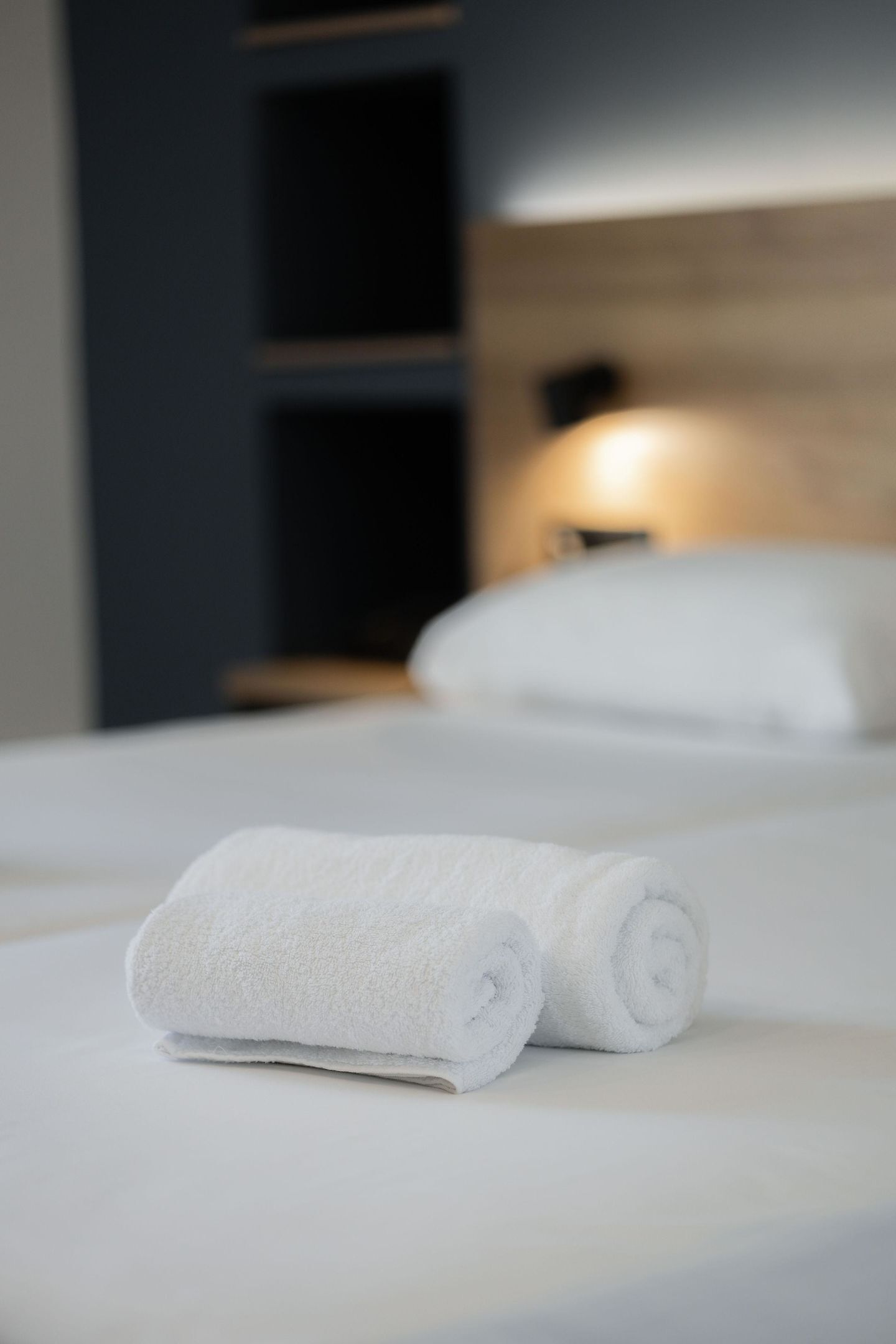 A neatly made bed with two rolled white towels in front.