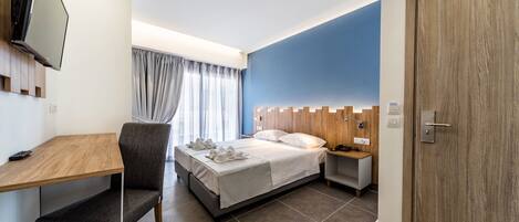 A modern hotel room with a bed, a desk, a chair, a TV, and a wardrobe.