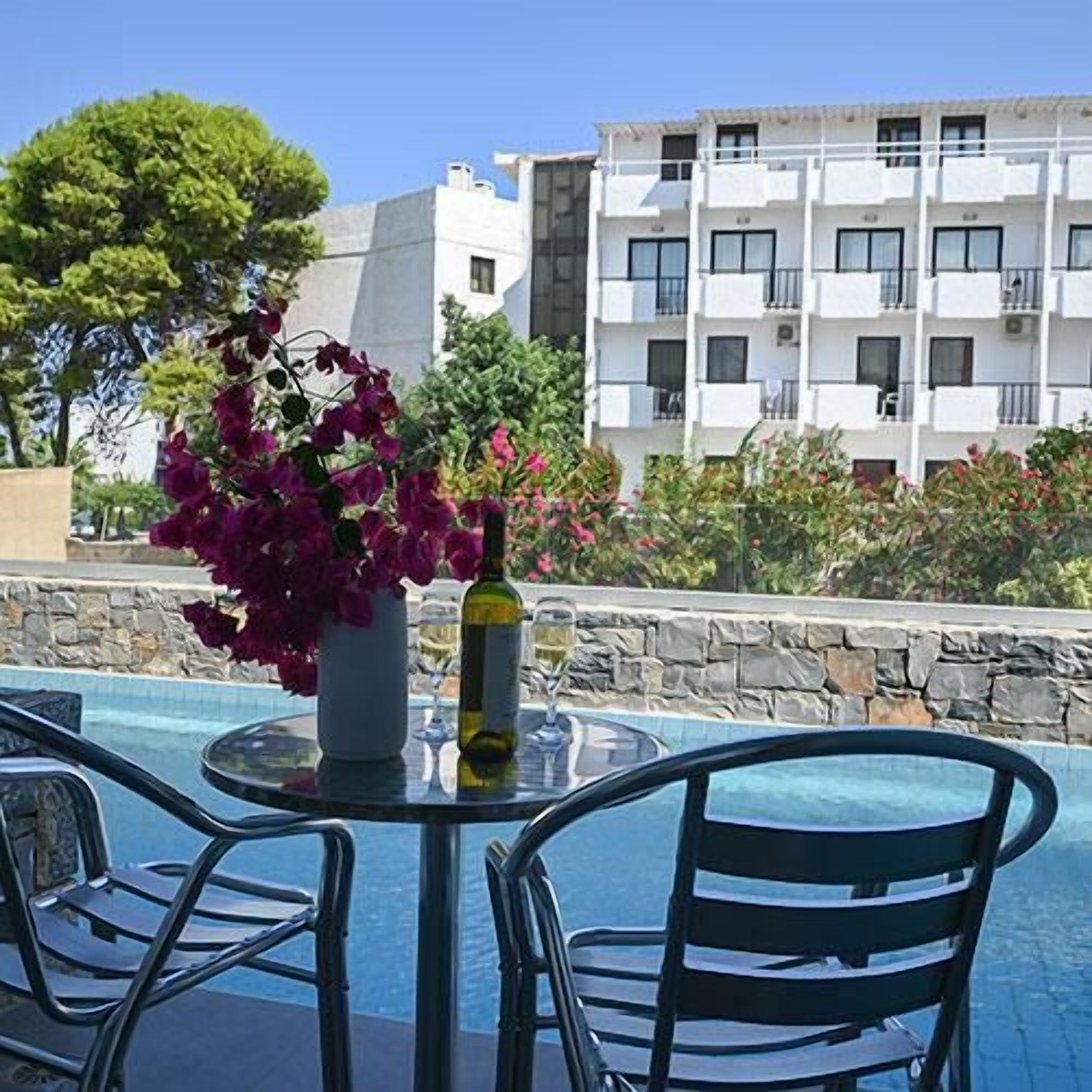 A poolside area with a table and chairs, a bottle of wine, and a vase of flowers.