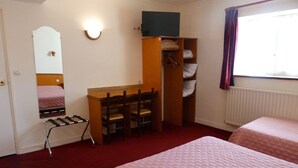 Habitación de hotel con cama, escritorio con sillas, armario, espejo y ventana con cortinas.