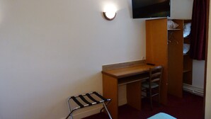 Habitación pequeña con cama, escritorio, silla, televisor montado en la pared y armario.