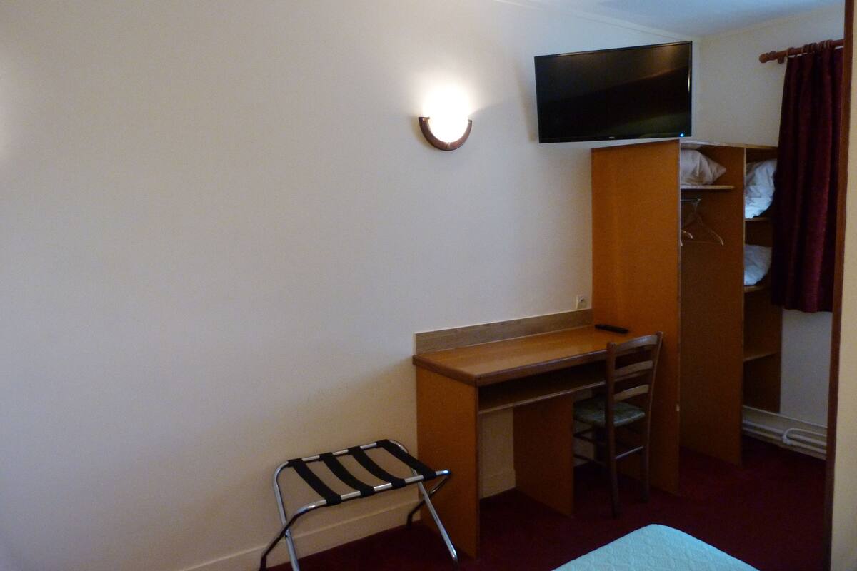 Une petite pièce comprenant un lit, un bureau, une chaise, un téléviseur fixé au mur et une armoire.