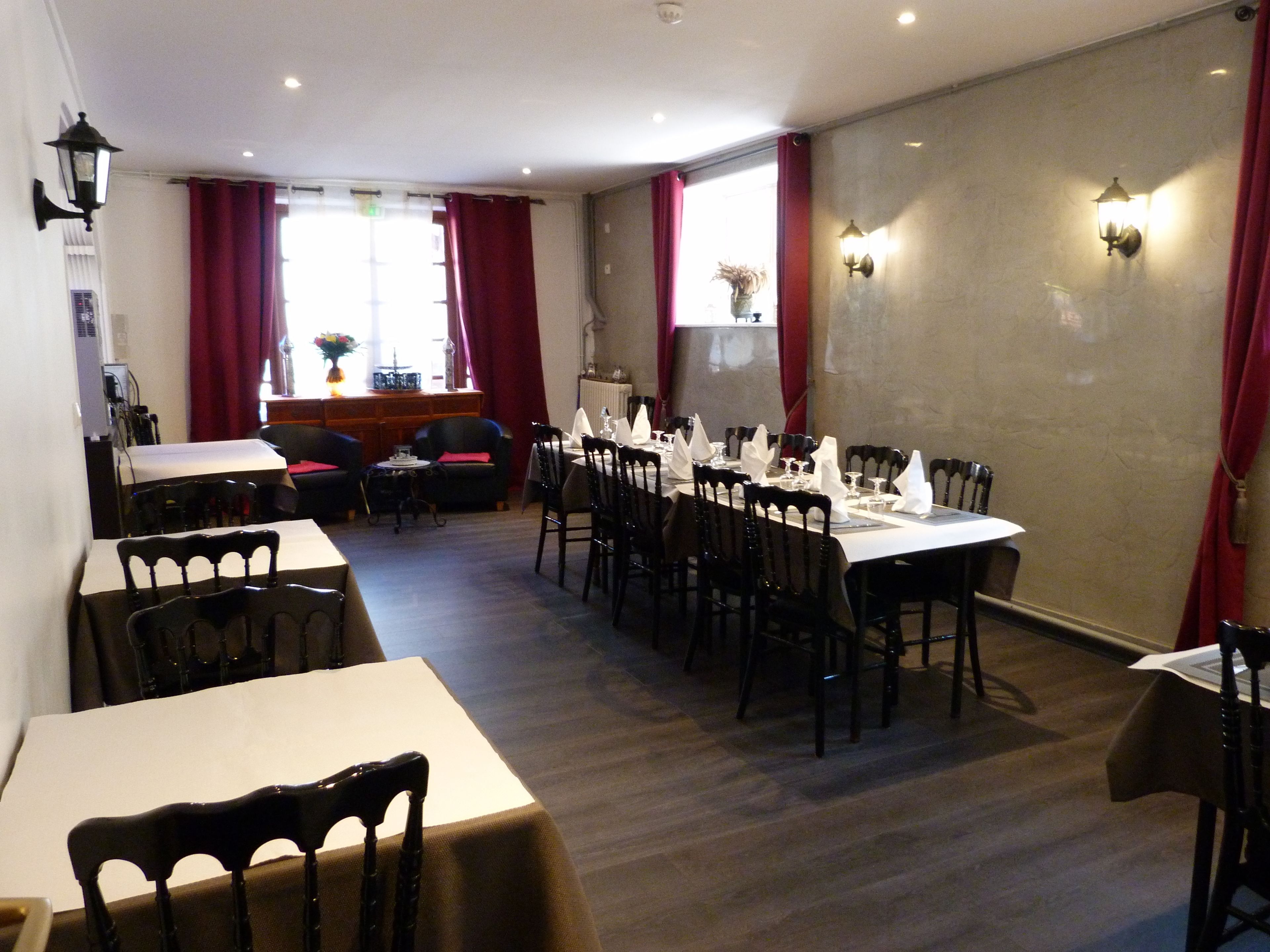 Un comedor con varias mesas dispuestas para el servicio, sillas alrededor y vistas al resto del comedor a través de una ventana con cortinas rojas.