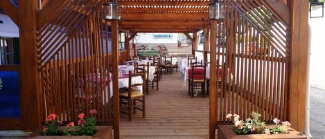 Una pérgola de madera al aire libre con mesas y sillas, un letrero que dice 'PARKING' y macetas con flores.