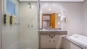 A modern bathroom with a glass shower enclosure, a sink with a granite countertop, and a white bathtub. - Alameda Felice Hotel (Gramado)