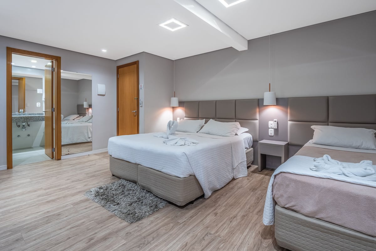 Ein modernes Hotelzimmer mit zwei Betten, einer Holztür, einem Spiegel und einem kleinen Badezimmer, das durch eine geöffnete Tür sichtbar ist.