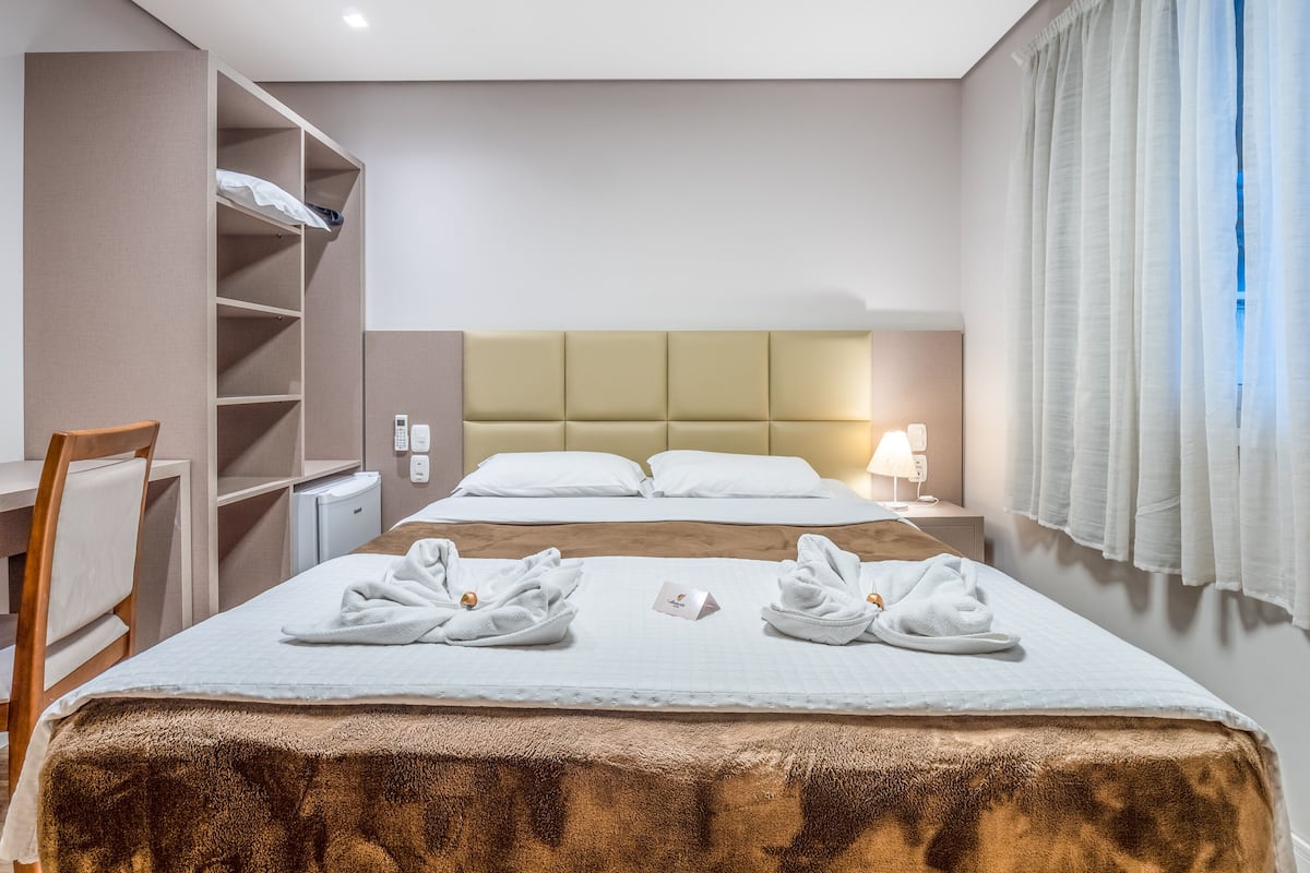 Ein Hotelzimmer mit zwei Betten, einem Schreibtisch, einem Stuhl, einem Kleiderschrank und einem Badezimmer.