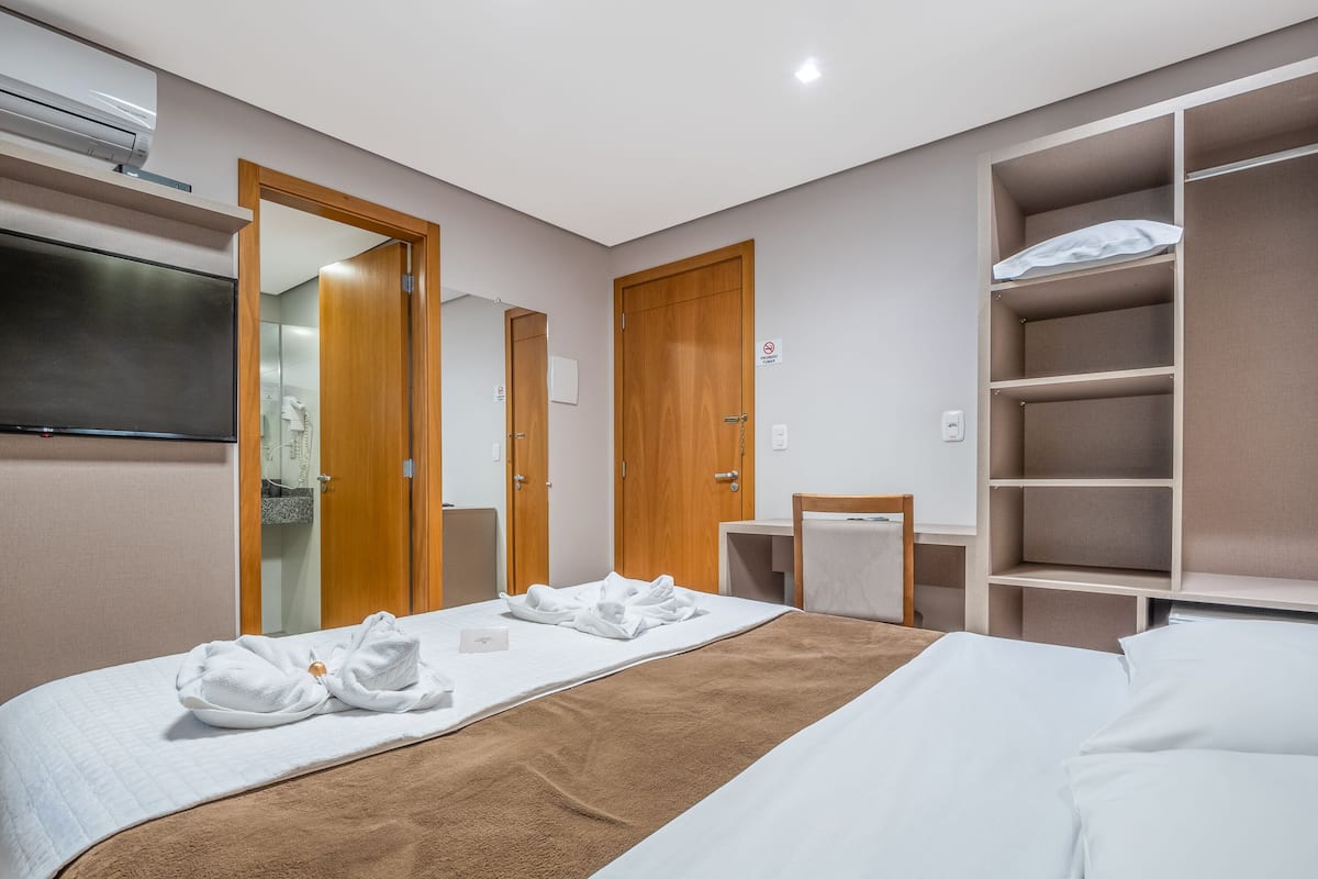 Ein Hotelzimmer mit einem Bett, einem Fernseher, einem Kleiderschrank und einem Regal mit Handtüchern.