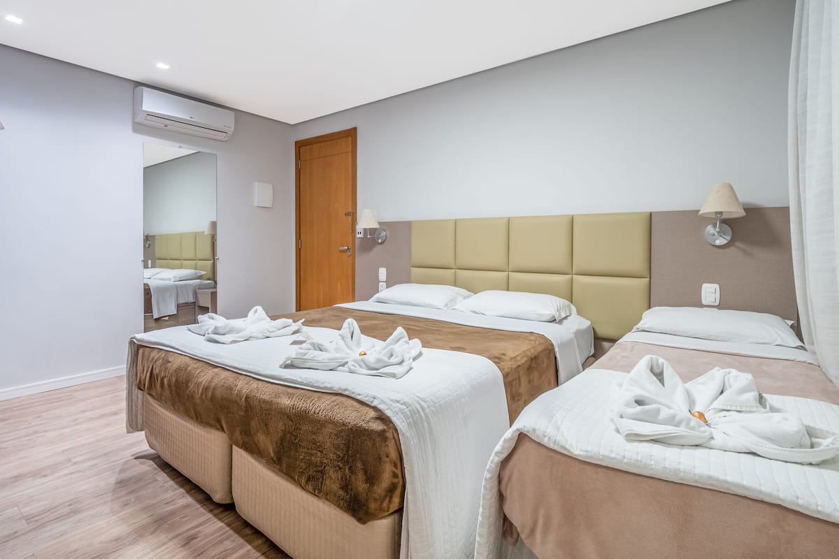 Ein Hotelzimmer mit drei Betten, einer Holztür, einem Spiegel und einer Deckenleuchte.
