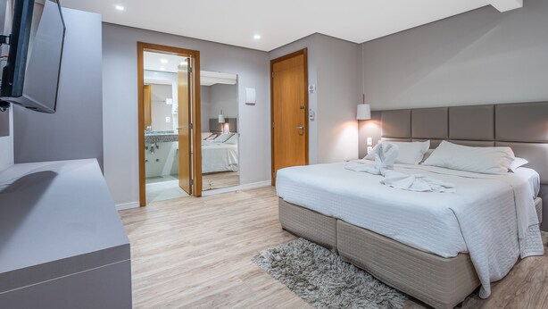 A modern hotel room with a large bed, a TV mounted on the wall, and a bathroom visible through an open door. - Alameda Felice Hotel (Gramado)