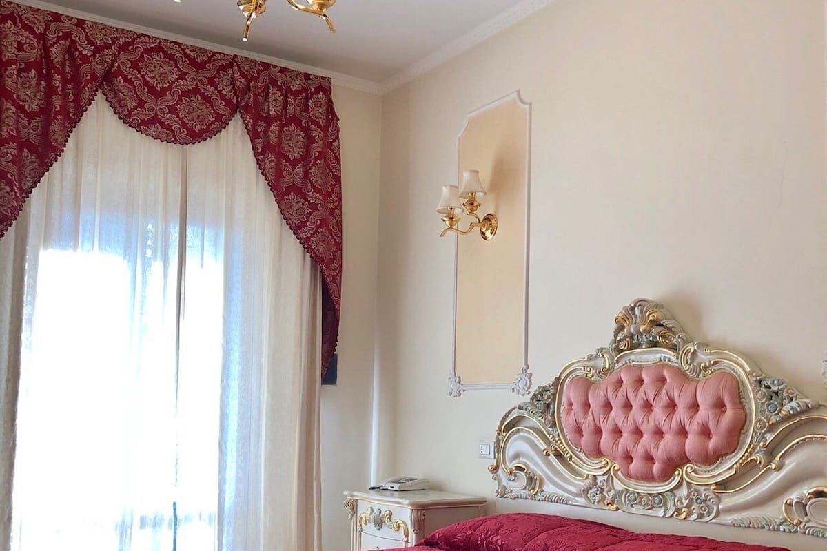 A bedroom with a large bed, a chandelier, a mirror, and a nightstand.